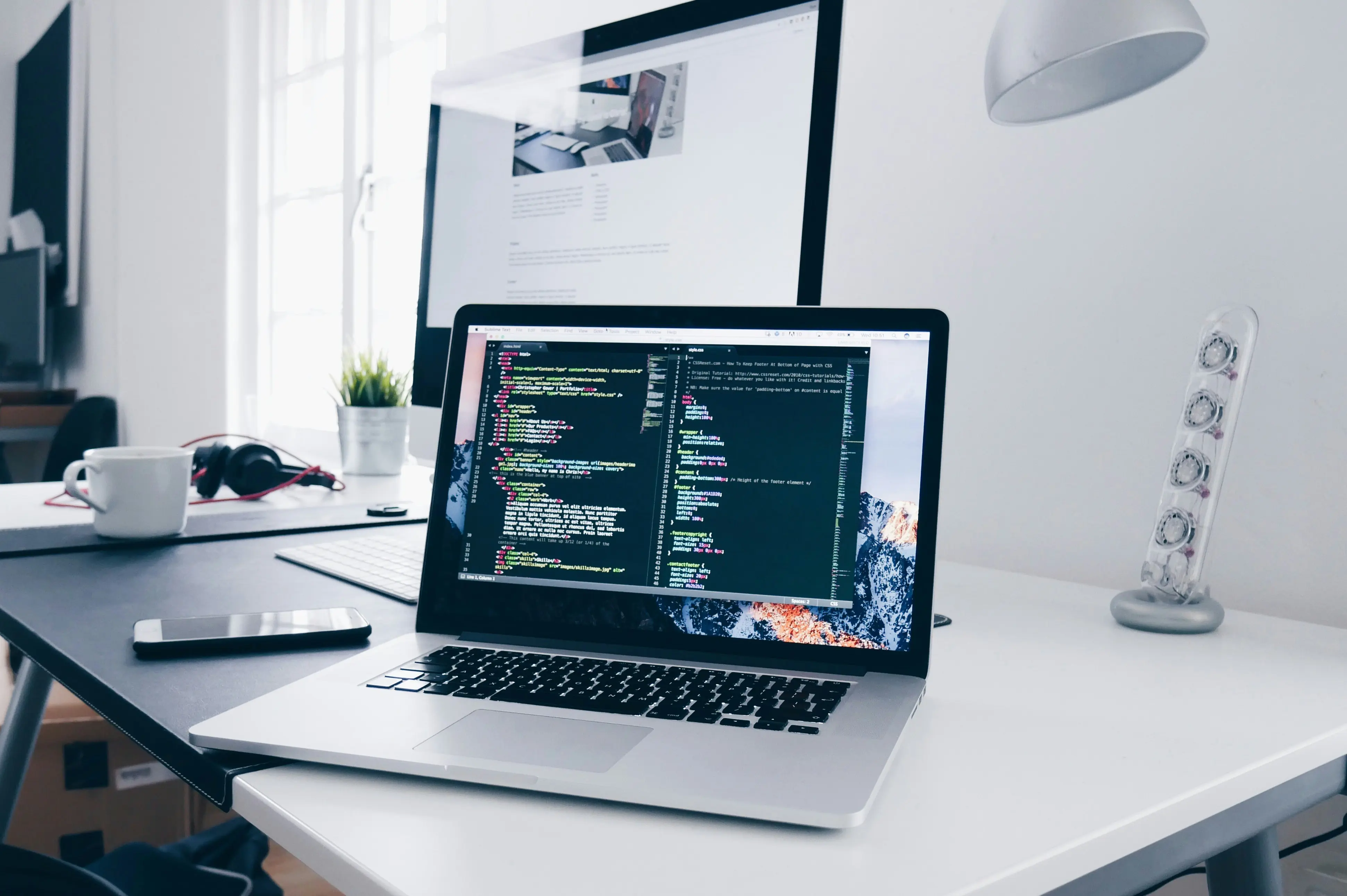 A macbook with a window opened, showing lines of code, standing on a white desk.